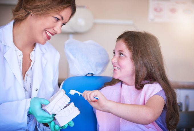 Dentist, woman and teaching girl for teeth, model or consulting for oral wellness in hospital. Child, orthodontist and 3d mould with toothbrush, cleaning or health with learning for hygiene at clinic.