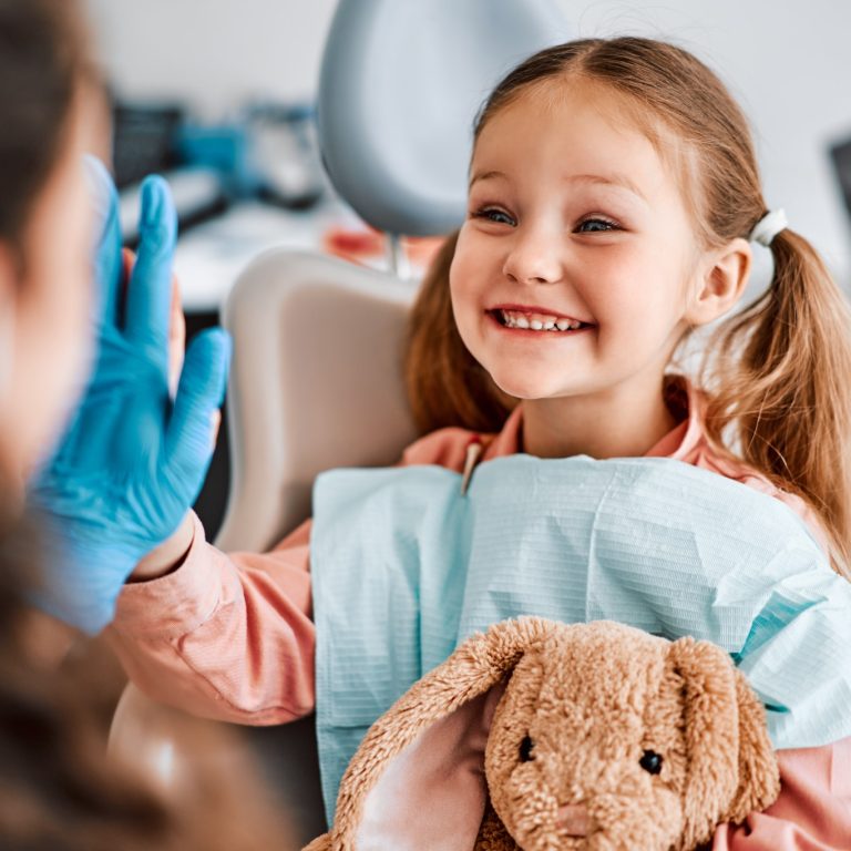 At the doctor's appointment. A candid emotional photo of a child sitting in a dental chair, holding a toy rabbit and cheerfully giving a high-five to the nurse.
