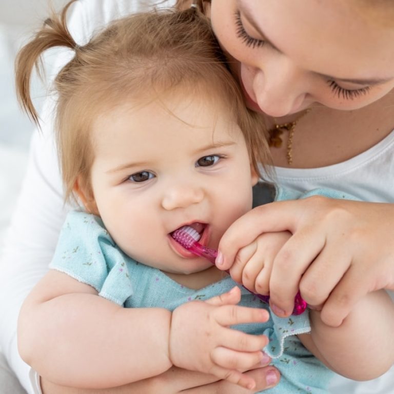 Mother,Brushing,Baby's,First,Tooth,With,Toothbrush,While,Child,Laughing.