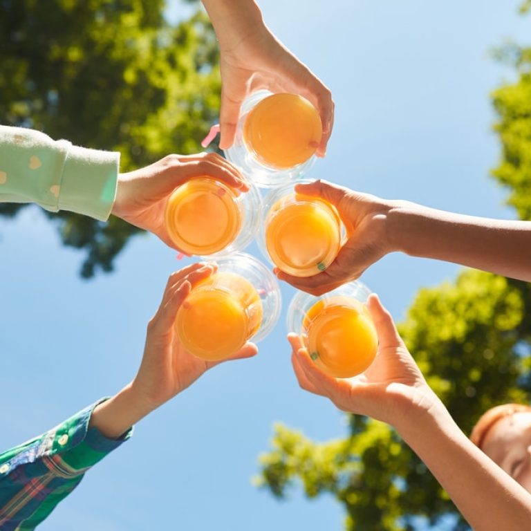 Low,Angle,Close,Up,Of,Kids,Holding,Glasses,With,Orange
